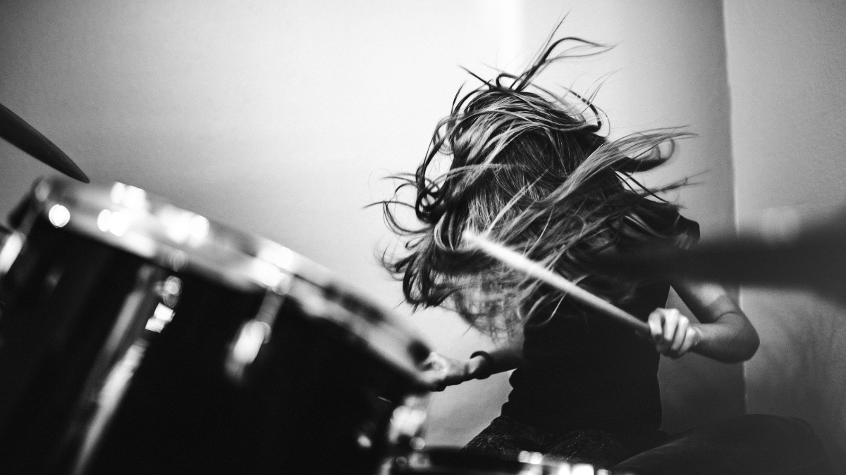 Black and white photo of a drummer playing aggressively, with their hair flying around.